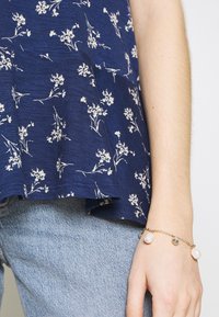 Navy blue floral top with white prints, lightweight fabric, relaxed fit, and a slight flared hem. Silver and pearl bracelet on wrist.