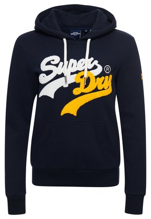 Granatowa bluza z kapturem z białymi troczkami, przednią kieszenią oraz logo "Super Dry" w białych i żółtych teksturowanych literach.