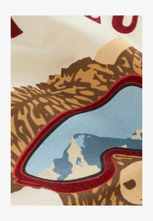 Tessuto in cotone con un design di orso, con pelliccia marrone testurizzata, riflesso blu delle montagne negli occhiali da sole e accenti bordati di bordeaux.