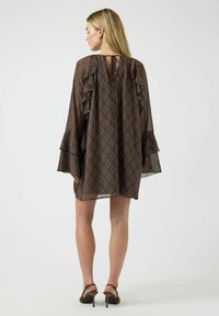 Brun rutete kjole med volangsleeves, en keyhole-åpning bak og knappedetalj. Laget av lett stoff, med en løs og flytende passform.