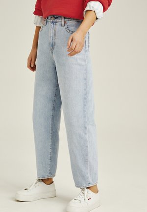 Person wearing light blue high-waist straight jeans, white sneakers, red sweatshirt, and rolled-up striped shirt sleeves.