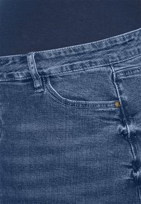 Jeans de denim, azul médio, design tradicional de cinco bolsos, detalhes de costura subtil e uma textura suave com acabamentos em metal.