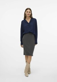 Marineblauwe button-up shirt met lange mouwen, gecombineerd met een grijze gestreepte kokerrok en beige suède laarzen tot de knie.