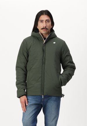Veste isolée verte avec capuche, dotée d'une fermeture éclair à l'avant et d'un logo discret sur la poitrine. Portée sur un jean bleu. Texture lisse.