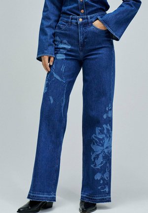Jeans de mezclilla de pierna ancha en azul profundo con detalles de estampado floral en una tonalidad más clara. Tienen una cintura alta y un dobladillo sutilmente deshilachado.