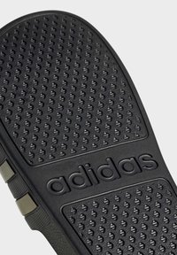 Black rubber slide sole with textured grip pattern, featuring the Adidas logo embossed. Accents of gray on the side.