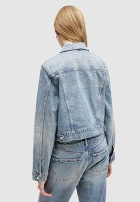 Giacca di jeans azzurro chiaro con un design corto, polsini con bottone e dettagli sulla cucitura del dietro, mostra una texture sbiadita e leggermente usurata.