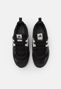 Zapatillas deportivas negras con parte superior de malla, detalles texturizados, cordones negros y acentos del logo blanco de Adidas en la lengüeta y los lados.