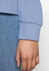 Puño de sudadera azul claro hecho de suave tela de algodón, con un dobladillo limpio y una textura suave, combinado con material de mezclilla.