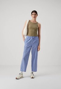 Oliwkowy top na ramiączkach zestawiony z luźnymi spodniami w niebiesko-białe paski. Całość dopełniają białe trampki i beżowa torba na ramię.