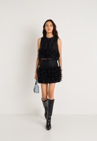 Μαύρη αμάνικη μπλούζα και κοντή φούστα με υφή και ρίγες. Το μοντέλο κρατά μια ανοιχτό μπλε τσάντα και φορά γυαλιστερές μαύρες μπότες ως το γόνατο.