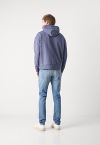 Felpa blu navy con cappuccio regolabile, materiale in misto cotone, polsini e orlo a coste, abbinata a jeans azzurri e sneakers beige.