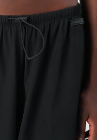 Shorts de sport noirs avec un waistband élastique, cordon de serrage ajustable et une petite étiquette de logo. Présentent un tissu lisse et une coupe ample.