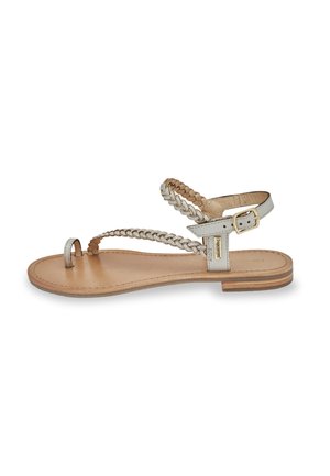 Sandalo piatto argento metallizzato con cinture intrecciate e design minimalista. Sottopiede in pelle con suola marrone chiaro e fibbia regolabile.