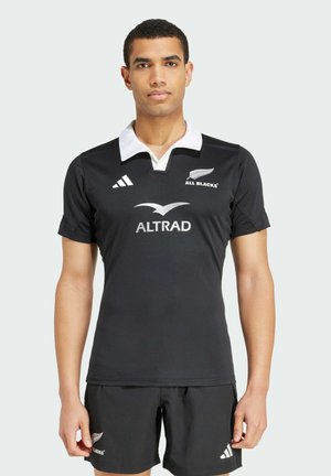 Maillot de rugby noir avec un col blanc, comportant les logos "ALL BLACKS", "ALTRAD" et adidas. Fabriqué en tissu lisse et sportif. Les shorts sont noirs.