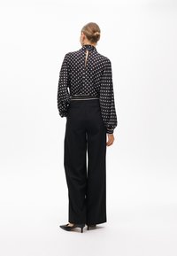 Black polka dot blouse with a high collar, puff sleeves, and a back keyhole detail, paired with high-waisted black wide-leg trousers.