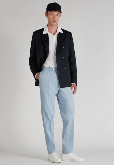 Granatowa, dwurzędowa marynarka, biała koszulka polo, jasnoniebieskie spodnie i białe sneakersy. Gładkie kolory z klasycznymi guzikami i detalami kieszeni.