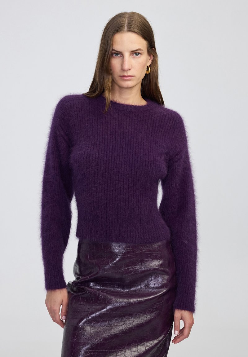 Pull tricoté violet à texture duveteuse avec manches longues et encolure ronde, associé à une jupe en cuir violet foncé brillante. Texture douce et coupe courte.