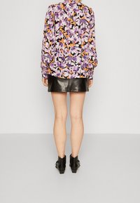 Blusa a maniche lunghe con un vivace motivo floreale in viola, giallo e arancione, abbinata a una mini gonna di pelle nera e stivaletti.
