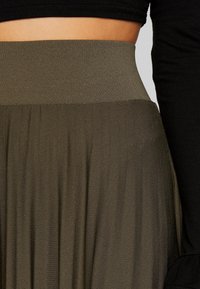 Gonna verde oliva con una vita ampia e liscia e tessuto fluido e strutturato. Il design presenta pieghe morbide. Top nero visibile lateralmente.