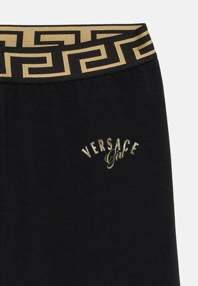 Juodos laisvalaikio kelnės su auksiniu juosmens diržu, puoštu graikų rakto raštu, ir "Versace Girl" logotipu metalinio aukso siuvinėjimu.
