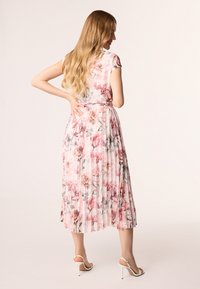 Robe plissée à fleurs avec un tissu rose pastel orné de roses et de motifs de fleurs, des manches courtes, et une taille cintrée.