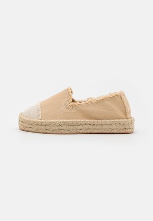 Beige slip-on espadrille med frynset kant, vævet jutesål og lysefarvet tåhætte, vist fra siden på hvid baggrund.