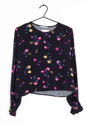 Blouse à manches longues en tissu doux de couleur marine, ornée de motifs floraux vibrants en rose, violet, jaune et bleu, avec des poignets froncés et un ourlet arrondi.