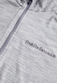 Felpa sportiva grigia, con tessuto testurizzato, zip a lunghezza totale e logo ricamato "PeakPerformance" sulla parte sinistra del petto.