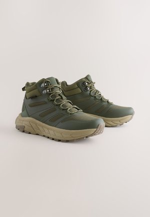 Rohelised matkajalatsid kõrge säärega, tekstuurse sünteetilise pealsega, tugevdatud silmade ja vastupidava tallaga, mis tagab haarduvuse.