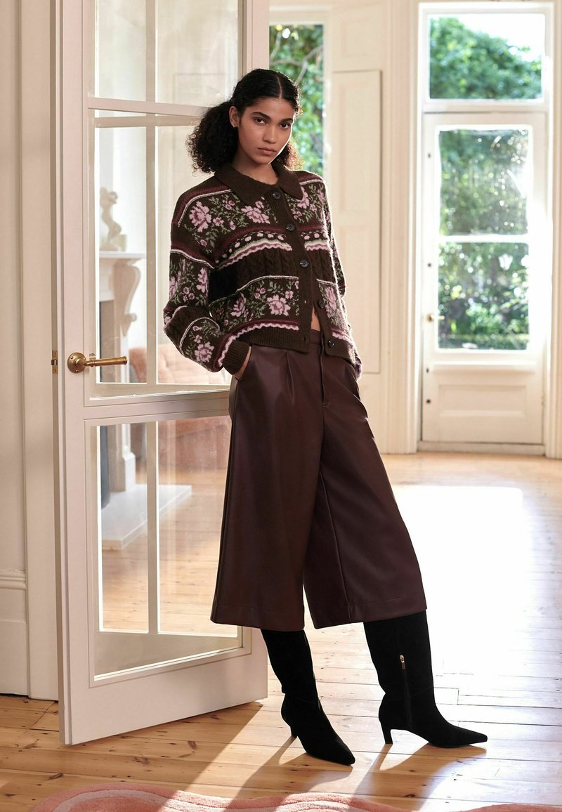 Gebreide cardigan met bloemenpatroon in donkerbruin, gecombineerd met hoge, bruine neplederen wijde broek en zwarte kniehoge laarzen.