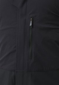 Schwarze leichte Jacke mit einer Reißverschlusstasche an der Seite, glatter Textur und Nahtdetails am Saum.