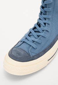 Høye sneakers i blå kanvas med forsterket tofarge blå semsket tåhette, teksturert gummisåle og flate blå lisser.