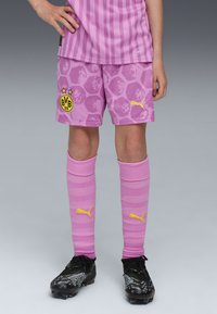 Violet jalkapallosortsit kuusikulmaisella kuviolla, keltainen BVB-logo, yhdistettyinä matching vaaleanpunaisiin sukkiin, joissa on keltainen Puma-logo ja mustiin nappulakenkiin.