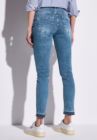 Vaaleansiniset farkkutrikoot, joissa on viisi taskua, rispaantuneet helmat ja sileä pinta, yhdistettyinä valkoisiin lenkkareihin.