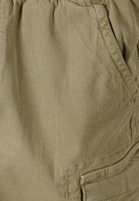 Close-up van beige stoffen broek met een voorzak, stikdetails en een gestructureerd katoenmateriaal.