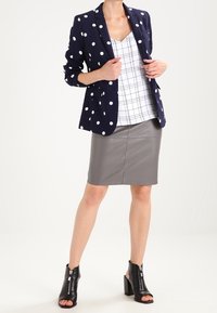 Námořnický blejzr s puntíky přes bílou kostkovanou blůzu, doplněný šedou tužkovou sukní a černými otevřenými kotníkovými botami. Hladké tkaniny.