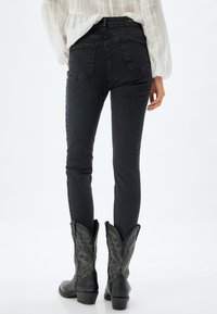 Jeans skinny in denim scuro con vita alta, caratterizzati da un classico design a cinque tasche, indossati con stivali da cowboy neri.