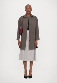 Grauer, knopfgleicher Mantel mit zwei vorderen Taschen, getragen über einem schwarzen Oberteil und einem hellgrauen Rock. Schwarze spitze Schuhe und eine weinrote Tasche. Glatte Textur.