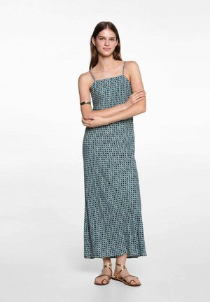 Abito lungo blu con motivo a griglia, spalline sottili e silhouette a trapezio. Indossato con sandali oro a cinturino alla caviglia, tessuto liscio.