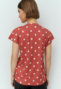 Chemise courte à manches rouges avec des pois blancs, encolure ronde et texture douce. La vue de dos montre une coupe décontractée et un ourlet arrondi.