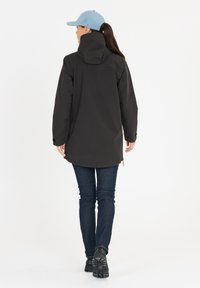Svart vattentålig jacka med huva, långa ärmar och sidodragkedjor. Kombinerad med mörk denimjeans och svarta skor. En ljusblå keps bärs.