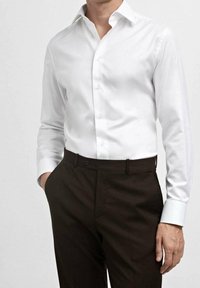 Witte blouse met een wijde kraag, lange mouwen en contrasterende lichtblauwe manchetten, gecombineerd met donkerbruine broek.