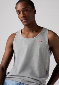 Débardeur en coton gris avec un col rond et un petit logo Levi's rouge sur la poitrine gauche. Le tissu a une texture lisse.