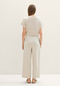 Conjunto de dos piezas beige que incluye una blusa de manga corta y pantalones de pierna ancha. Textura suave con un ajuste relajado, combinado con zapatos planos.