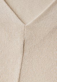 Ljust beige stickad tröja med V-ringning, jämn struktur och subtil ribbning längs kanterna.