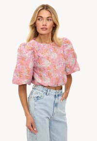 Top court à manches courtes en rose avec des motifs floraux, présentant des manches bouffantes et un tissu texturé. Associé à un jean taille haute bleu clair.