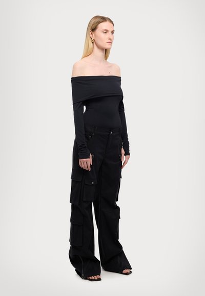 Top negru, cu umerii la vedere, cu mâneci lungi, asociat cu pantaloni cargo negri, lejeri, care au multiple buzunare și fermoare.
