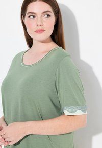 Groene top met korte mouwen heeft een ronde hals en kantaccenten op de mouwen. Zachte stof met een gladde textuur en subtiele glans.