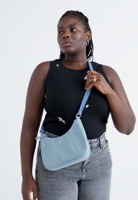 Light blue denim crossbody bag with a curved design, adjustable strap, and subtle logo. The bag is smooth with minimal accents.